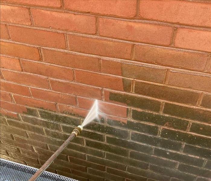 Power washer cleaning soiled brick wall. 