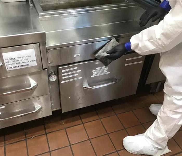 Employe cleaning commercial kitchen appliance. 