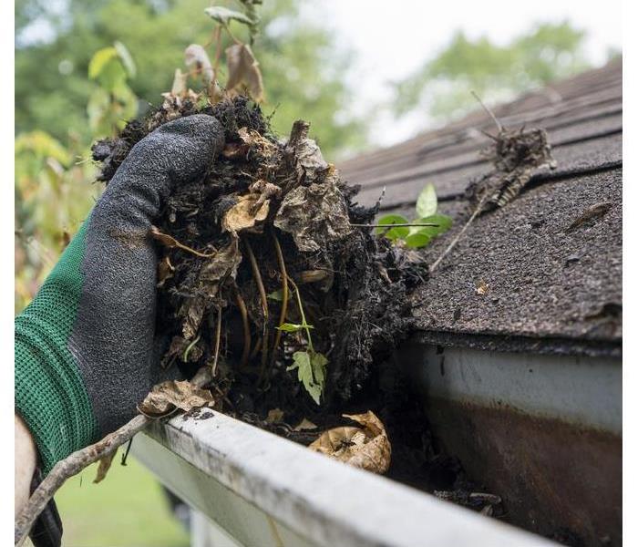 Hand with glove cleaning a dirty gutter