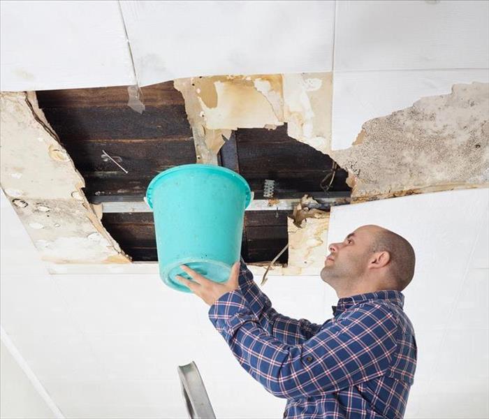 Man holding a bucket, while ceiling is leaking.