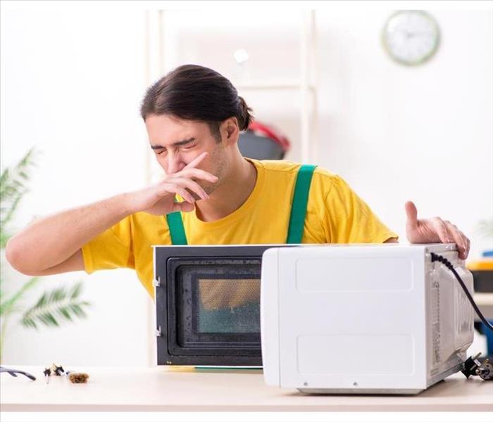 man covering his nose when opening a microwave oven